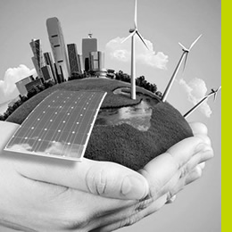 A hand holds a small globe featuring a city skyline, wind turbines, and solar panels, symbolizing sustainability and renewable energy.